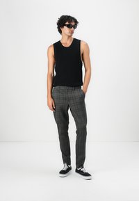 Schwarzes ärmelloses Top, graue Karo-Hose, schlanker Schnitt, dezentes Karomuster, kombiniert mit schwarzen Sneakern mit weißen Sohlen.
