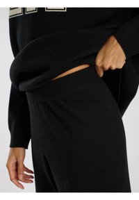 Svart stickad loungekläder-set med en avslappnad passform, som har en mjuk textur och elastisk midja. Toppdelen är något instoppad i byxorna.