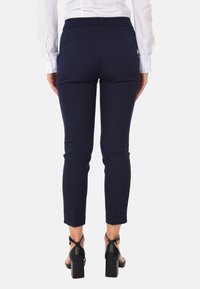 Pantaloni blu navy, aderenti, con una texture liscia, di lunghezza appena sopra la caviglia e due tasche posteriori. Indossati con sandali neri con tacco a blocco.