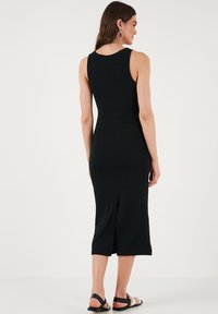 Crna rebrasta midi haljina bez rukava s prorezom na leđima. Ima usku siluetu i glatku teksturu. Jednostavan i elegantan dizajn.
