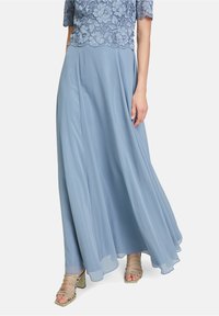 Kvinna i en svävande ljusblå chiffong maxi kjol med en blå spetsblus och ljusgröna sandaletter med klack.