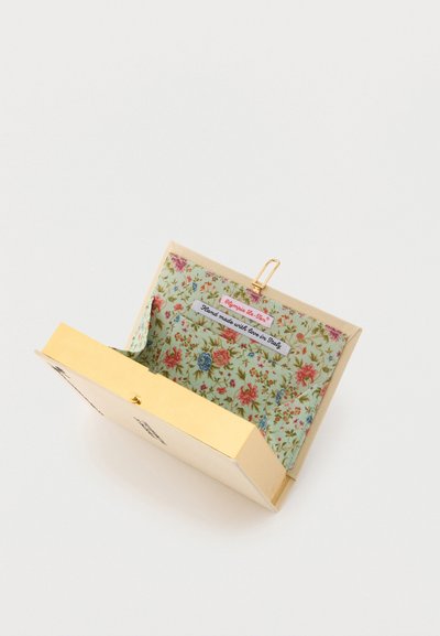 Cartera color crema abierta que muestra el interior de tela floral con etiquetas que dicen "Olympia Le-Tan" y "Hecho a mano con amor en Italia."