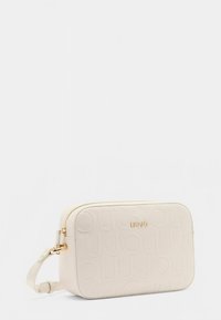 Kreemikas värvi kunstnahast kott reljeefse logoga, ristkülikukujuline, kuldsete detailidega ja reguleeritava rihmaga. Sile tekstuur, minimalistlik disain.