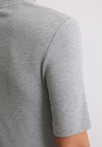 Szara, prążkowana koszulka z krótkim rękawem, prezentująca fakturowany materiał w dopasowanym fasonie. Dekolt jest okrągły z delikatnym wykończeniem.