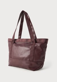 Temno rjava usnjena torba z ujemajočimi se tekstilnimi ročaji, pokončno stoji na beli podlagi.