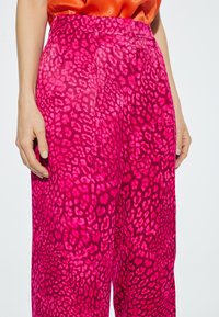 Roze panterprint broek met een ontspannen pasvorm, voorzien van plooien en een gladde textuur. Te zien in combinatie met een oranje satijnen top.