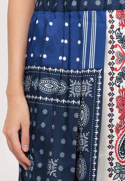 Braccio accanto a tessuto plissettato con pois blu e bianchi, strisce e intricati motivi floreali paisley rossi e neri.