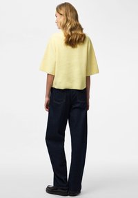 Yellow ribbed knit top with wide sleeves, paired with dark blue high-waisted jeans and black flat shoes. Smooth texture and relaxed fit.