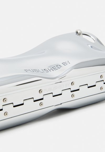 Metal harmonica with a shiny silver finish, curved design, engraved text "PUBLISHED BY," and visible hardware with a smooth texture.