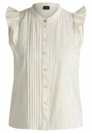 Mouwloze witte blouse met een knoopsluiting aan de voorkant, verticale plooien en rimpelaccenten op de schouders. Soepele textuur met verfijnde details.