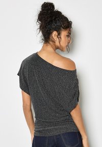 Asymetryczna czarna bluzka z teksturowanej tkaniny, z jednolitym ramieniem i marszczeniami w talii. Krótkie rękawy i luźny krój.