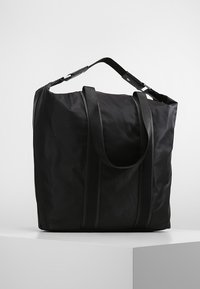 Zwarte nylon draagtas met twee stevige handgrepen, een zachte textuur en contrasterende verticale strepen aan de voorkant. Praktisch en ruim ontwerp.