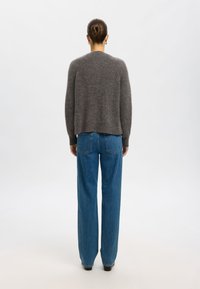 Grijze, gestructureerde gebreide trui met een ronde halslijn, gecombineerd met hooggetailleerde blauwe wijde jeans, gezien vanaf de achterkant.