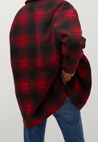 Rød og sort ternet oversized flannel skjorte med en buet kant og sænket skuldre, med lange ærmer og klassisk krave.