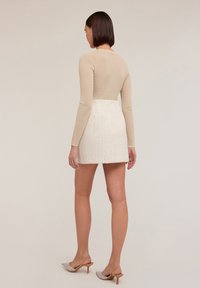 Top a maniche lunghe beige a coste abbinato a una mini gonna bianca con texture. Indossato con décolleté a punta impreziositi, che mettono in mostra una silhouette elegante.