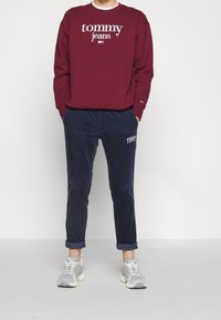 Felpa bordo con logo bianco "tommy jeans", abbinata a pantaloni in corduroy blu navy con ricamo "TOMMY". Sneakers grigie sportive.