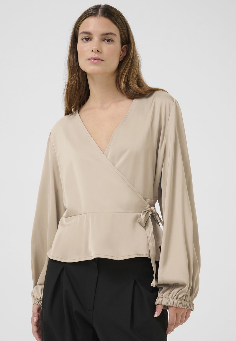 Blusa avvolgente beige in tessuto liscio, con maniche lunghe e polsini arricciati, e una fascia regolabile in vita.