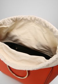 Oranžová kabelka z umělé kůže se soft tkaninou uvnitř. Obsahuje řasený vršek a vnitřní černou zipovou kapsu pro bezpečné uložení věcí.