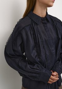 Marinebluse aus leichtem Stoff, mit Rüschensaum an den Ärmeln und knöpfbarem Frontbereich, voluminösen Ärmeln und klassischem Kragen.