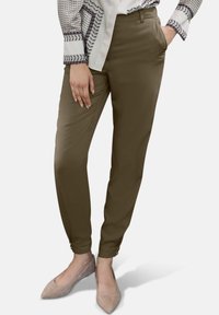 Olijfgroene broek met een tapered fit, voorzien van zijzakken en knoopaccenten bij de zoom, gecombineerd met grijze puntige flats.