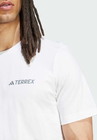 White cotton t-shirt featuring a grey "TERREX" logo on the left chest, short sleeves, and a crew neckline. Soft, smooth texture.