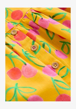 Tessuto giallo con motivi di ciliegie rosa e foglie verdi. Due bottoni di legno con dettagli a fiore su un design frontale plissettato.