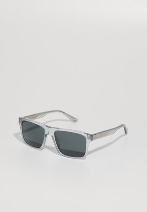 Transparent frame sunglasses with gray lenses, square shape, and metal accents on the arms, featuring a subtle logo detail.
