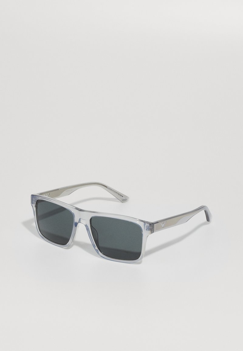 Ochelari de soare cu ramă transparentă, lentile gri, formă pătrată și accente din metal pe brațe, având un detaliu subtil cu logo.