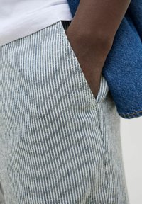 Lengvi, juostos tipo kelnių pagaminti iš lengvos medžiagos, su siaurais vertikaliais mėlynais ir baltais ruožais, šoniniu kišeniu ir džinsinio audinio akcentais.