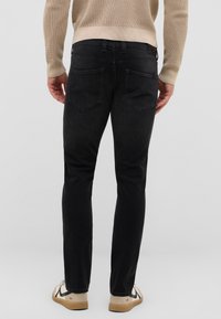 Jeans de mezclilla negra con un corte slim, con dos bolsillos traseros y una cintura de media altura. Llevados con un suéter beige y calzado casual.