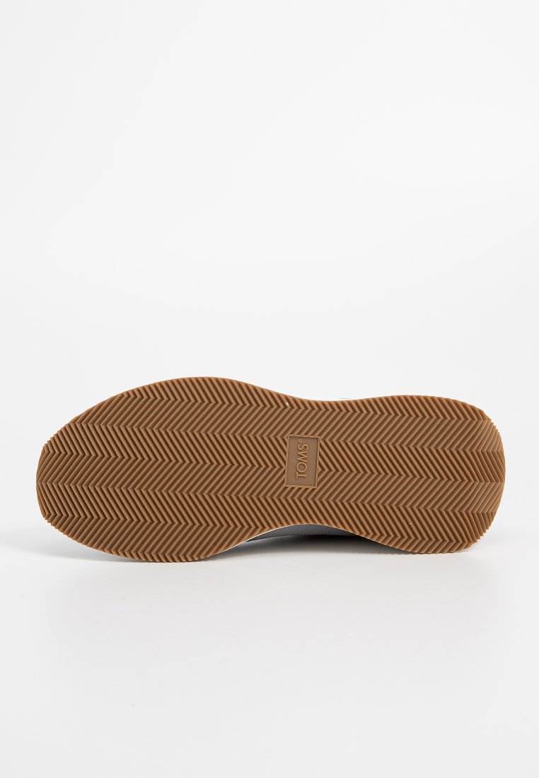 Semelle en caoutchouc brun avec un motif en chevrons et un logo en relief. Le fond plat et flexible offre traction et durabilité.