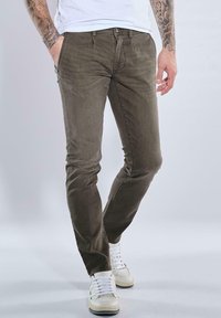 Khaki slim-fit jeans in stretch cotton with a smooth texture. Features five pockets and a button-fly closure, paired with white sneakers.