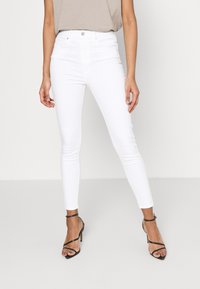 Vita högmidjade skinny jeans gjorda av ett stretchigt bomullsmaterial, med en främre knappstängning och sömlös design.