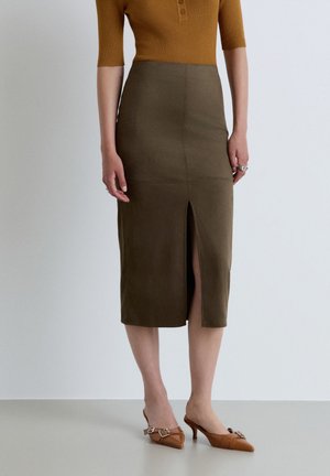 Donna con top marrone a coste, gonna midi verde oliva scuro con spacco frontale e tacchi slingback marroni con punta appuntita e dettaglio fibbia.