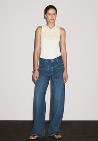 Lys beige, ærmeløs top parret med højtsiddende, vidde ben, blå denimjeans med to baglommer og en lige pasform.