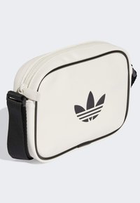 Witte synthetische tas met een zwart logo met drie strepen, rechthoekige vorm, ritsluiting en een contrasterende zwarte schouderband en afwerking.