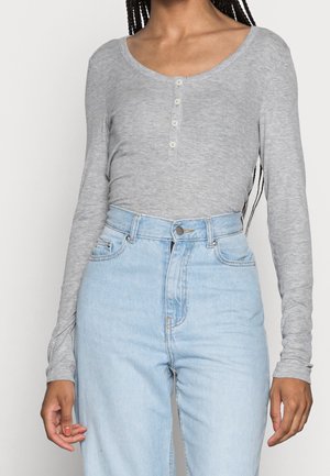 Femme portant un haut gris clair côtelé à manches longues ajusté avec des boutons et un jean taille haute bleu clair.