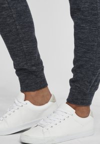 Hallid hallid puuvillased joggersid kitsaste varrukatega, milles on ühendatud valged madalad tossud, millel on ümmargune nina ja tekstuuriga lukk. 