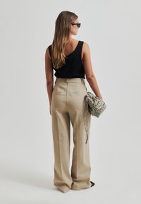 Pantaloni beige a vita alta con gamba larga, abbinati a un top nero senza maniche e una borsa a tracolla grigia con motivo. Tessuto morbido.