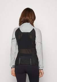 Veste légère noire et grise avec dos en mesh, capuche et poignets élastiques ; dotée d'accents réfléchissants et d'une coupe ajustée.