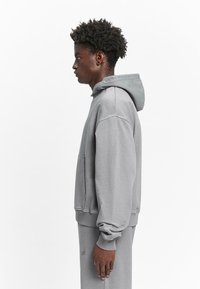 Gray hooded sweatshirt with a front pocket, loose fit, and ribbed cuffs. Fabric appears soft and textured, designed for comfort.