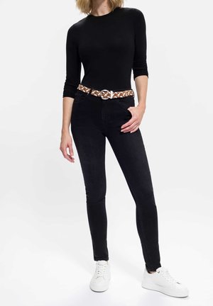 Jeans neri aderenti con cintura intrecciata marrone e bianca e scarpe da ginnastica bianche, caratterizzati da una texture liscia e una silhouette slim.