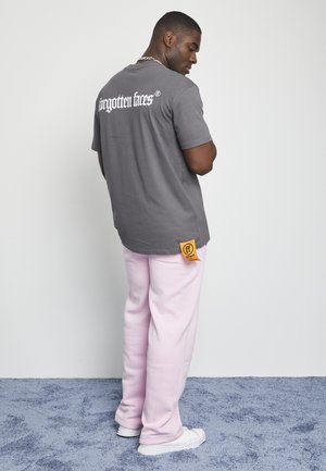 Gray t-shirt with "forgotten faces" logo printed in white on the back. Paired with light pink sweatpants and white sneakers. Orange tag visible.