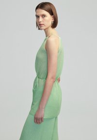 Abito verde chiaro senza maniche con un motivo a trama, vita regolabile con cordoncino e silhouette fluida. Tessuto liscio e design a vestibilità rilassata.