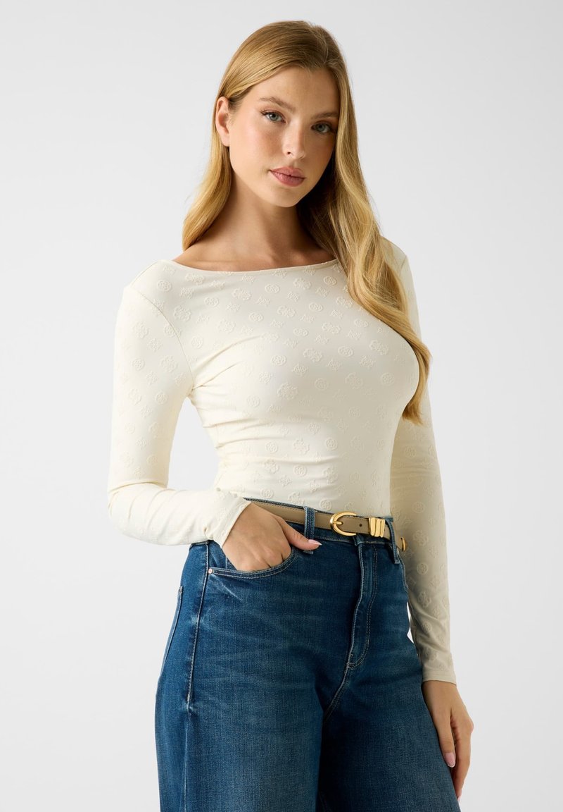 Crèmewit top met lange mouwen en een gestructureerd patroon, ronde halslijn, gecombineerd met een hooggetailleerde blauwe spijkerbroek en een tankleurige riem met een gouden gesp.