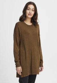Tunic tricotat maro cu mâneci lungi, gât rotund și fante laterale. Prezintă accente cu dungi pe umeri și o croială lejeră.