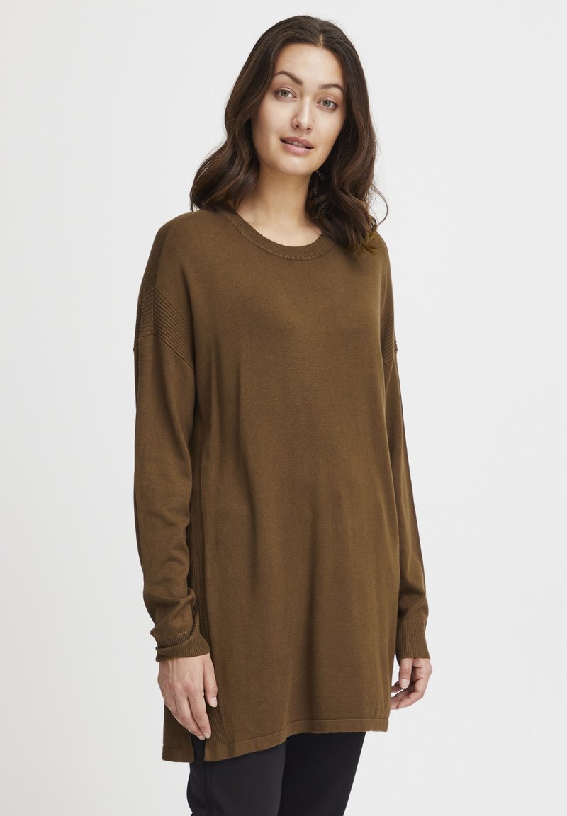 Tunic tricotat maro cu mâneci lungi, gât rotund și fante laterale. Prezintă accente cu dungi pe umeri și o croială lejeră.