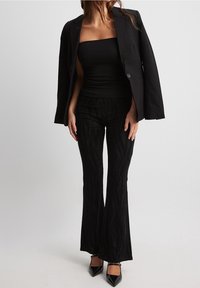 Zwart aansluitend strapless top gecombineerd met een op maat gemaakte zwarte blazer, en wijde, gestructureerde zwarte broek met metalen accenten. Elegante hakken maken de look compleet.