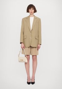 Beige oversized blazer with large lapels, two buttons, and front pockets. Paired with beige shorts and a small cream handbag with gold lettering.