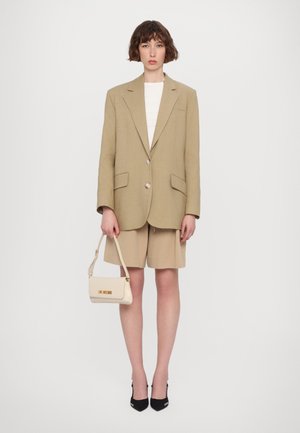 Blazer oversize beige avec de grands revers, deux boutons et des poches avant. Associé à un short beige et un petit sac à main crème avec lettrage doré.